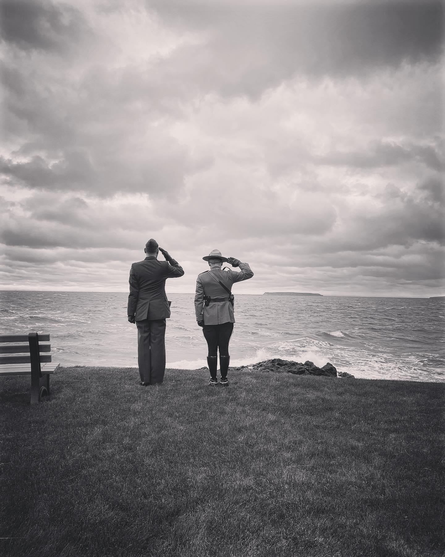 Two men engaged in a career transition discussion while standing on a bench next to the ocean.