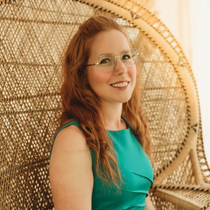 Kelly in glasses sitting in a wicker chair.